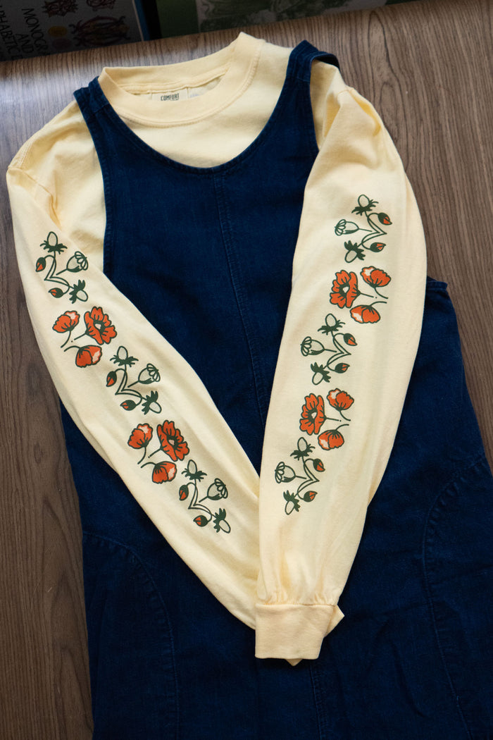 Butter yellow long-sleeved t-shirt with orangey red and green poppy floral pattern layered under a denim pinafore dress